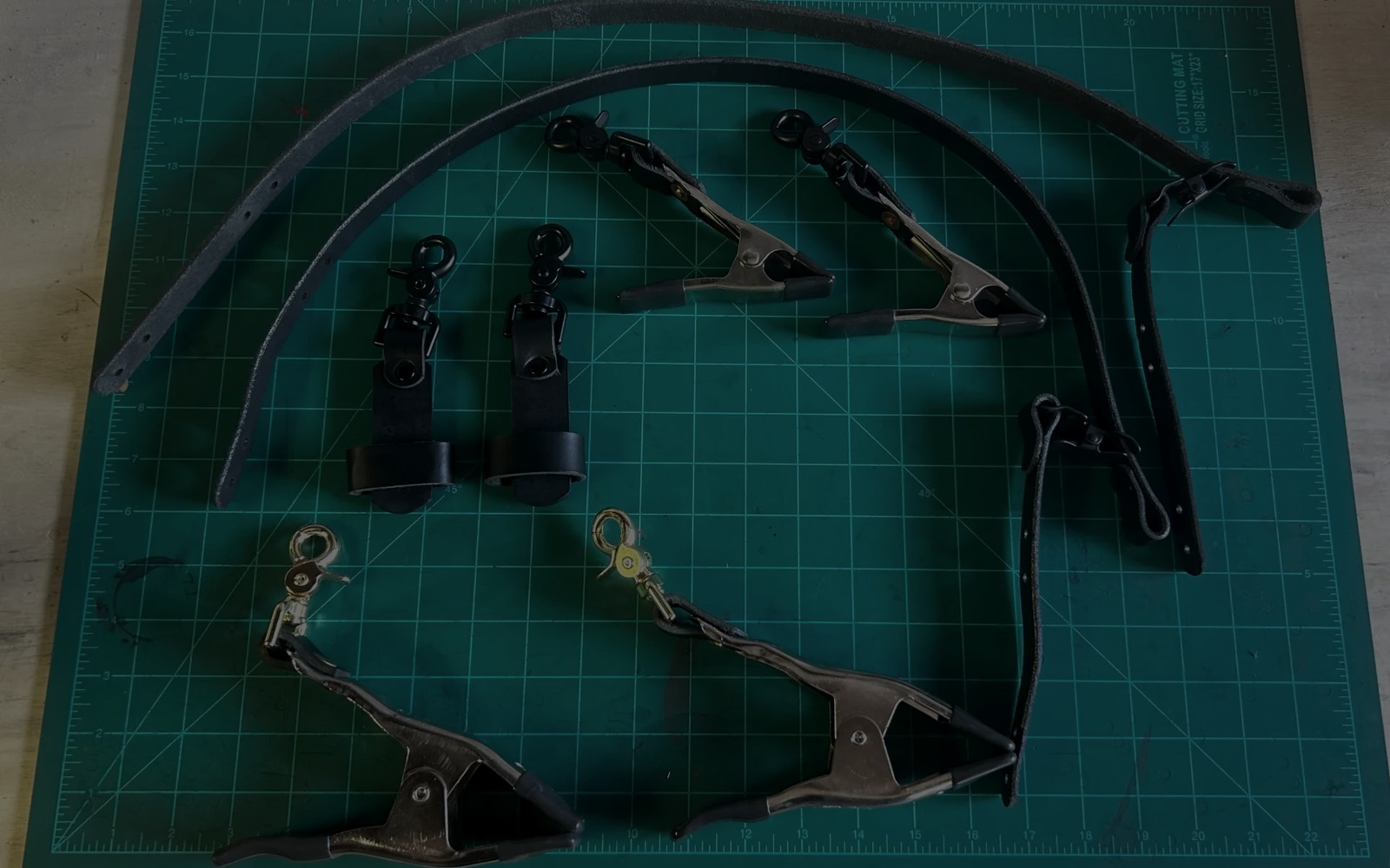 Handmade leather fire service straps and glove clips arranged on a workshop cutting mat